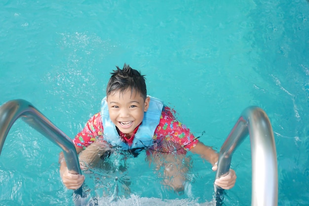 Aziatische kinderjongen oefent om te zwemmen en water te spelen in het blauwe zwembad