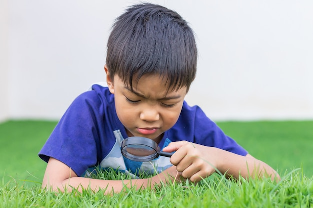 Aziatische kindjongen die en met vergrootglas op de bloemboom en de groene vloer van het grasgebied kijken kijken. avontuur, ontdekkingsreiziger en lerend kind.