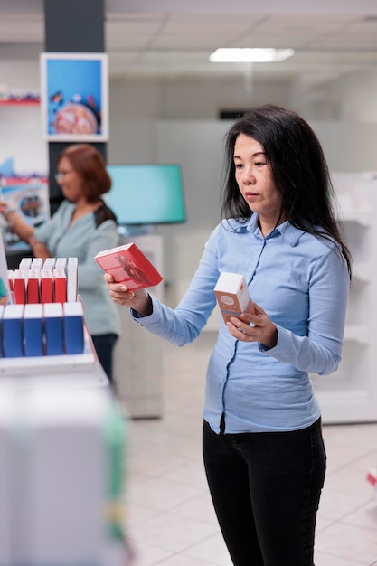 Aziatische klant die medicijnen wil kopen in de apotheek voor de gezondheidszorg, kijkend naar geneesmiddelen en farmaceutische benodigdheden. Vrouw in medische drogisterij met pillendozen op planken.