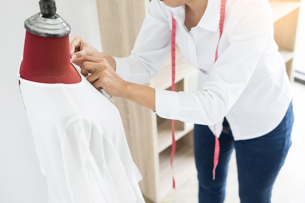 Aziatische kleermaker past kledingstuk ontwerp op mannequin in werkplaats.