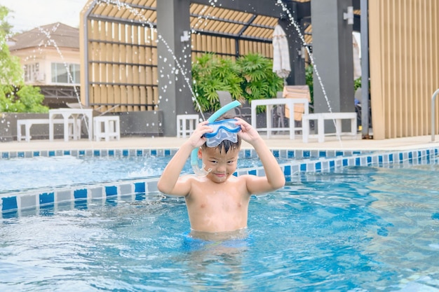 Foto aziatische kleine jongen in zwembril en snorkel leren zwemmen in het buitenzwembad in de zomerdag