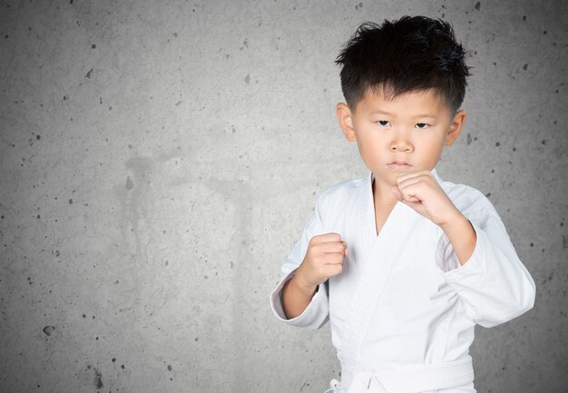 Aziatische kleine karatejongen in witte kimono op achtergrond