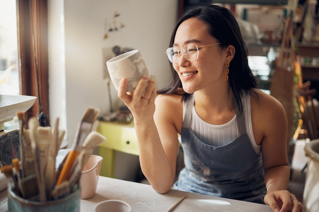 Aziatische kunstenaar en vrouw als kleine ondernemer blij met ontwerp en product tijdens een workshop Aardewerkmok en kleibeeldhouwwerk door creatieve startup vrouw glimlachend en tevreden door kunst