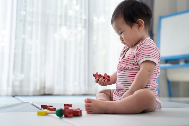 Aziatische leuke baby die en een klein stuk speelgoed op zachte mat thuis zit speelt.