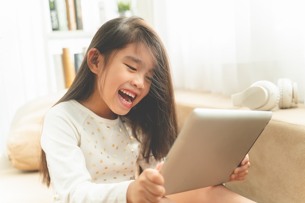 Aziatische Leuke kind speelspelen met een tablet en glimlachend terwijl thuis het zitten op bank