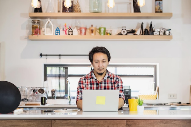 Aziatische man aan het werk vanuit huis met technologie laptop en mobiele telefoon in de keuken kamer