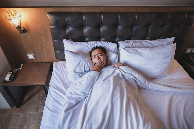 Aziatische man die deken gebruikt terwijl hij op een bed ligt