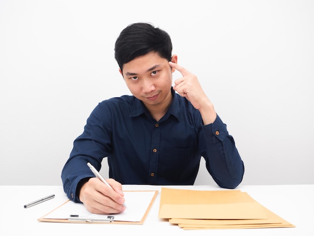 Aziatische man die document op tafel schrijft en met de vinger naar zijn hoofd wijst om concept te denken