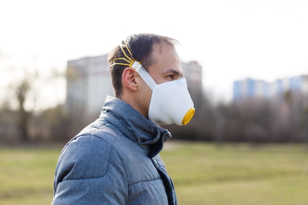 Aziatische man die het gezichtsmasker draagt als gevolg van luchtvervuiling - Jonge volwassene op park met vervuilingsmasker - persoon die beschermt tegen luchtverontreiniging of coronavirus of covid-19 door een masker te dragen.