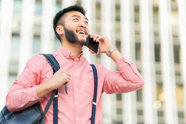 Aziatische man die lacht terwijl hij buiten met de mobiel praat