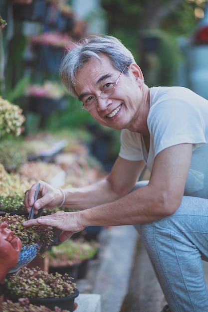 Aziatische man die lacht van geluk en zorgt voor kamerplant in de eigen tuin