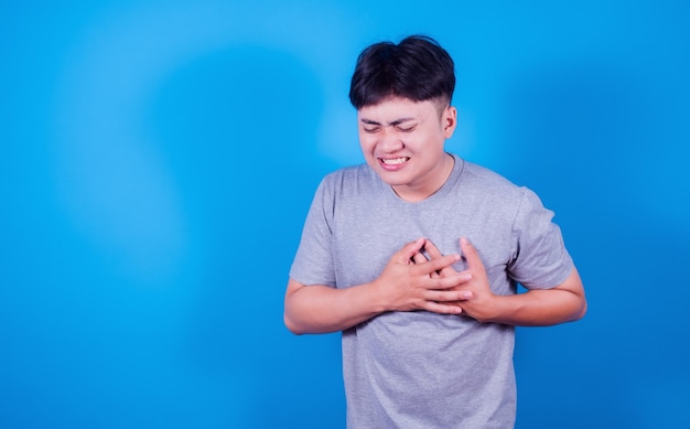 Aziatische man die op de borst drukt met een pijnlijke uitdrukking op een blauwe achtergrond, hartziekte. Gezondheidszorg en gezondheidsprobleem concept