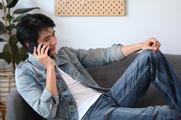 Aziatische man die op mobiele telefoon praat terwijl hij op een comfortabele bank rust