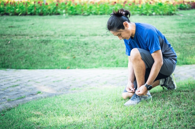 Aziatische man die sneakers bindt Maak je klaar om te oefenen door te joggen voor gezondheid in het park