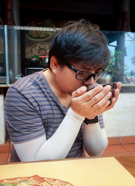Aziatische man die soep uit zwarte kom vasthoudt en eet aan tafel in restaurant