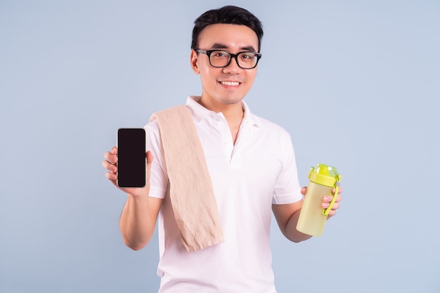 Aziatische man die sportkleding draagt en een waterfles, een sportschool en een yogaconcept vasthoudt