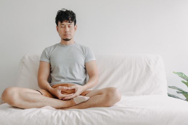 Aziatische man doet meditatie op de bank in zijn appartement