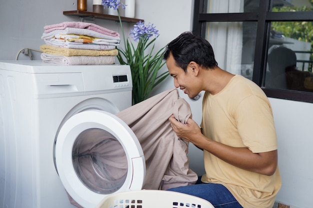 Aziatische man doet was thuis laden van kleren in de wasmachine ruikt het linnen