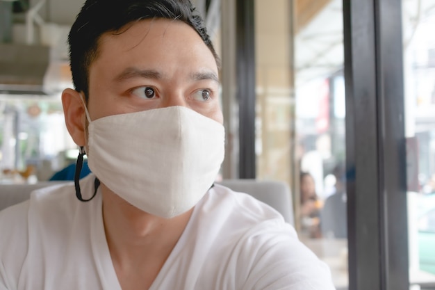 Aziatische man draagt een wit masker ter bescherming van het Covid-virus in een openbaar café.