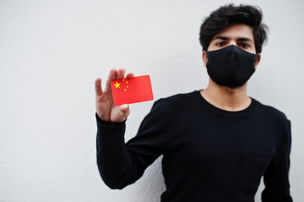 Aziatische man draagt helemaal zwart met gezichtsmasker houdt de vlag van China in de hand geïsoleerd op wit. Coronavirus land concept.