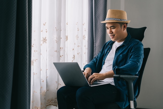 Aziatische man gebruikt zijn laptop om online te werken bij het raam, concept werk vanuit huis