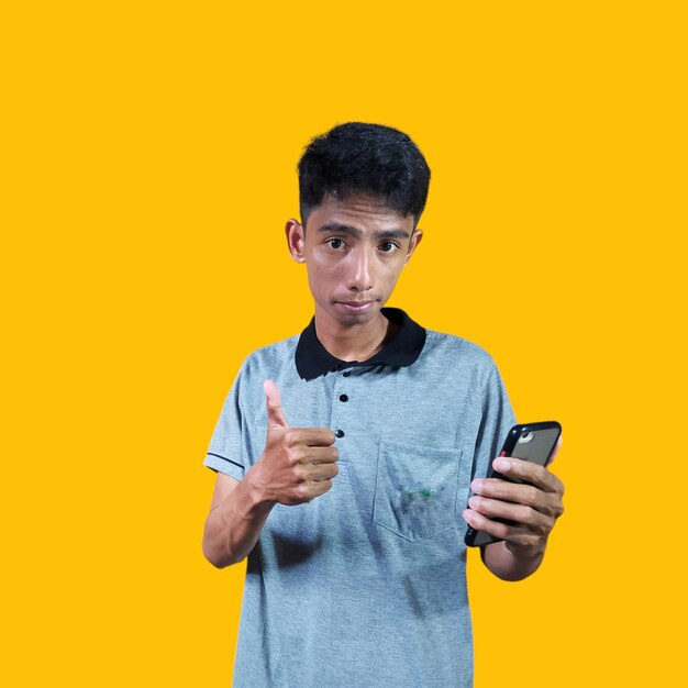 Aziatische man glimlachend gezicht met okay gebaar met smartphone geïsoleerd op blauwe achtergrond