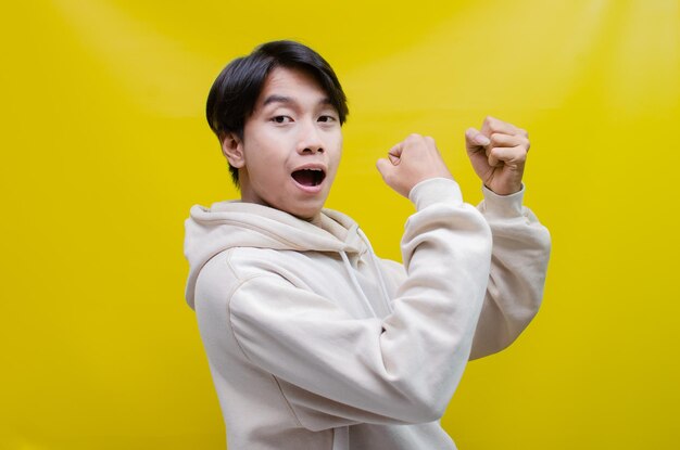 aziatische man in beige hoodie danst vrolijk en steekt zijn vuist op om de overwinning te vieren