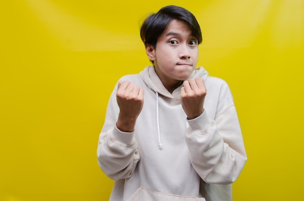 aziatische man in beige hoodie danst vrolijk en steekt zijn vuist op om de overwinning te vieren