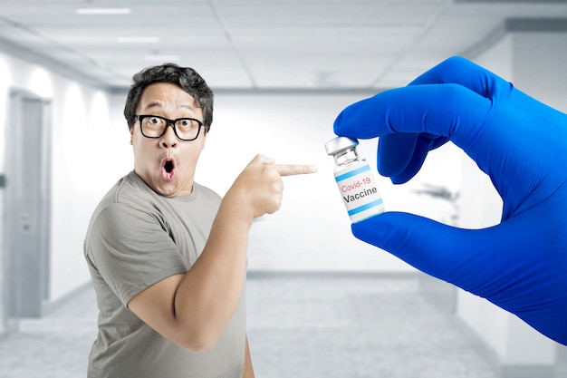 Aziatische man in bril wijzend naar de hand van de gezondheidswerker met handschoenen met covid 19-vaccins voor vaccinatie