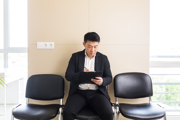 Aziatische man in de wachtkamer zittend op een stoel bij de receptie van het kantoorcentrum