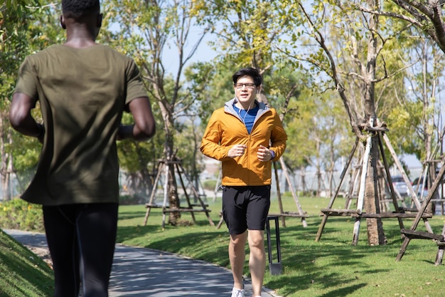 Aziatische man in gele hoodie joggen en rennen naast de weg in het park op herfstochtend.