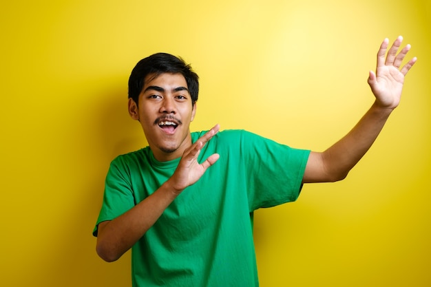 Aziatische man in groen t-shirt glimlachend en vrolijk dansend, blij uiting gevend aan het vieren van goed nieuws overwinning winnend succes gebaar tegen gele achtergrond