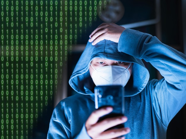 Aziatische man in hoodie en masker hackt Iets van een mobiele telefoon bedoeld voor wazige foto's heeft digitale nummers nummer één met nul