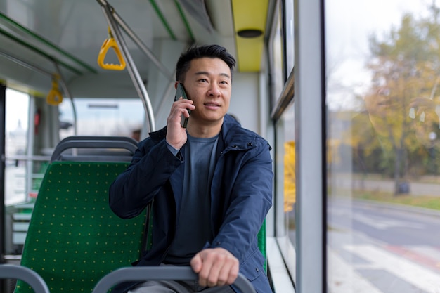 Aziatische man in openbare buspassagier die plezier heeft met praten op mobiele telefoon, in vrijetijdskleding