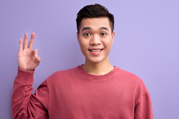 Aziatische man in vrijetijdskleding met ok gebaar op camera, glimlachend