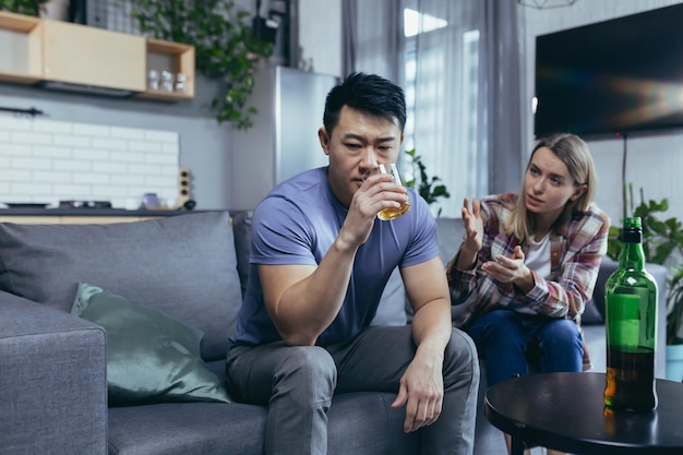 Aziatische man is een alcoholische drank die thuis sterke alcohol drinkt, zijn vrouw maakt ruzie met hem en probeert het multiraciale gezin thuis te bemoeien