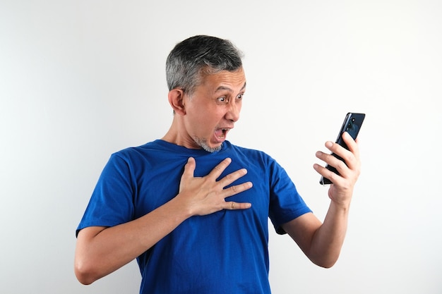 Aziatische man met blauwe t-shirt ziet er serieus uit met telefoon Slechte uitdrukking geschokt