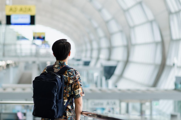 Aziatische man met een draagtas die staat en uitkijkt naar het reis- en vakantieconcept op de luchthaven