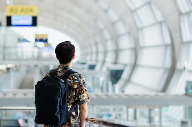 Foto aziatische man met een draagtas die staat en uitkijkt naar het reis- en vakantieconcept op de luchthaven