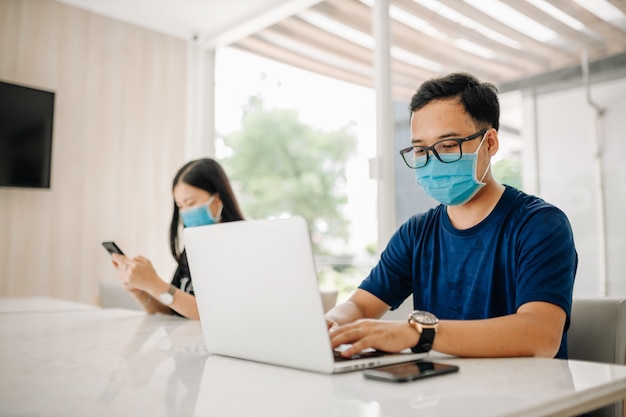 Aziatische man met een masker en met behulp van computer laptop in kantoor of klaslokaal voor preventie COVID-19 Virus.
