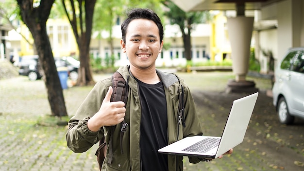 Aziatische man met een tas terwijl hij een laptop vasthoudt met ok gebaar