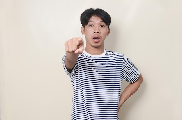 Aziatische man met gestreept shirt geschokte uitdrukking en voorkant tonend op geïsoleerde achtergrond