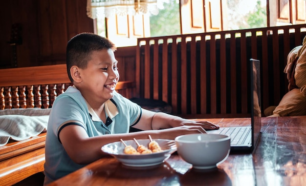 Aziatische man met laptop op houten tafel met junkfood thuis voor het raam