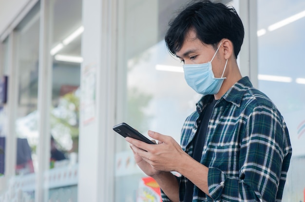 Aziatische man met mobiele telefoon zittend houdt sociale afstand, nieuw normaal na covid 19 of coronavirus