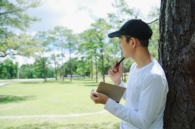 Aziatische man permanent en schrijven notitie onder dennenboom.