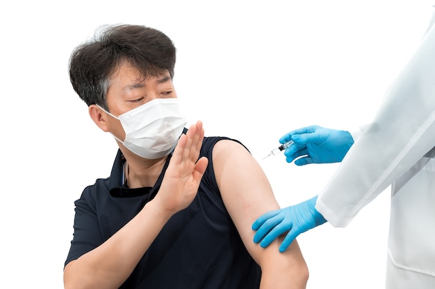 Aziatische man van middelbare leeftijd die medisch masker draagt en weigert het vaccin te injecteren.