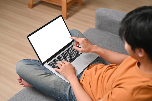 Aziatische man zit op de bank en gebruikt een laptopcomputer