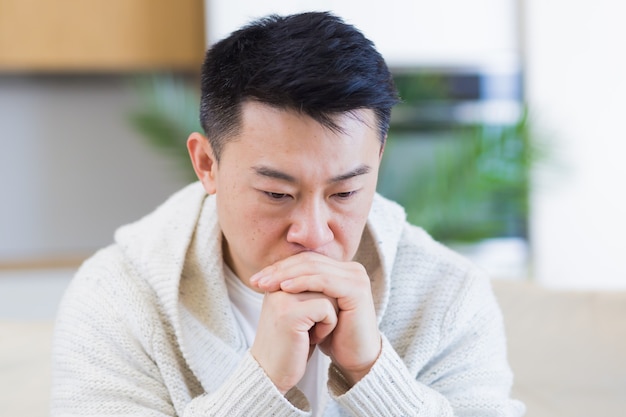 aziatische man zit thuis op de bank peinzend bezorgd over problemen en depressie