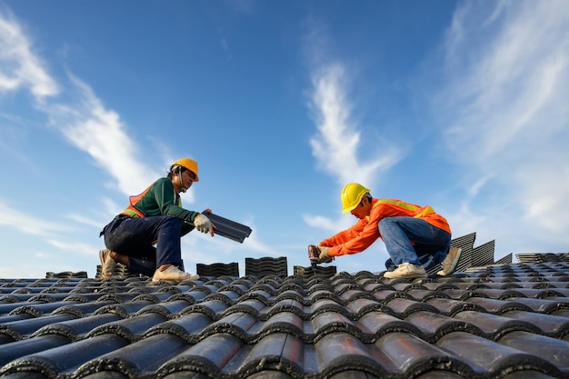 Aziatische mannelijke dakinstallateur Aziatische bouwvakkers op het dak Werk met een boor om keramische of cementdakschroeven op de bouwplaats te bevestigen