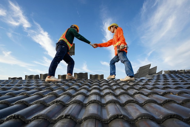 Aziatische mannelijke dakreparateur werkt samen als een team dat op het dak staat keramische of cementdakpannen op de bouwplaats